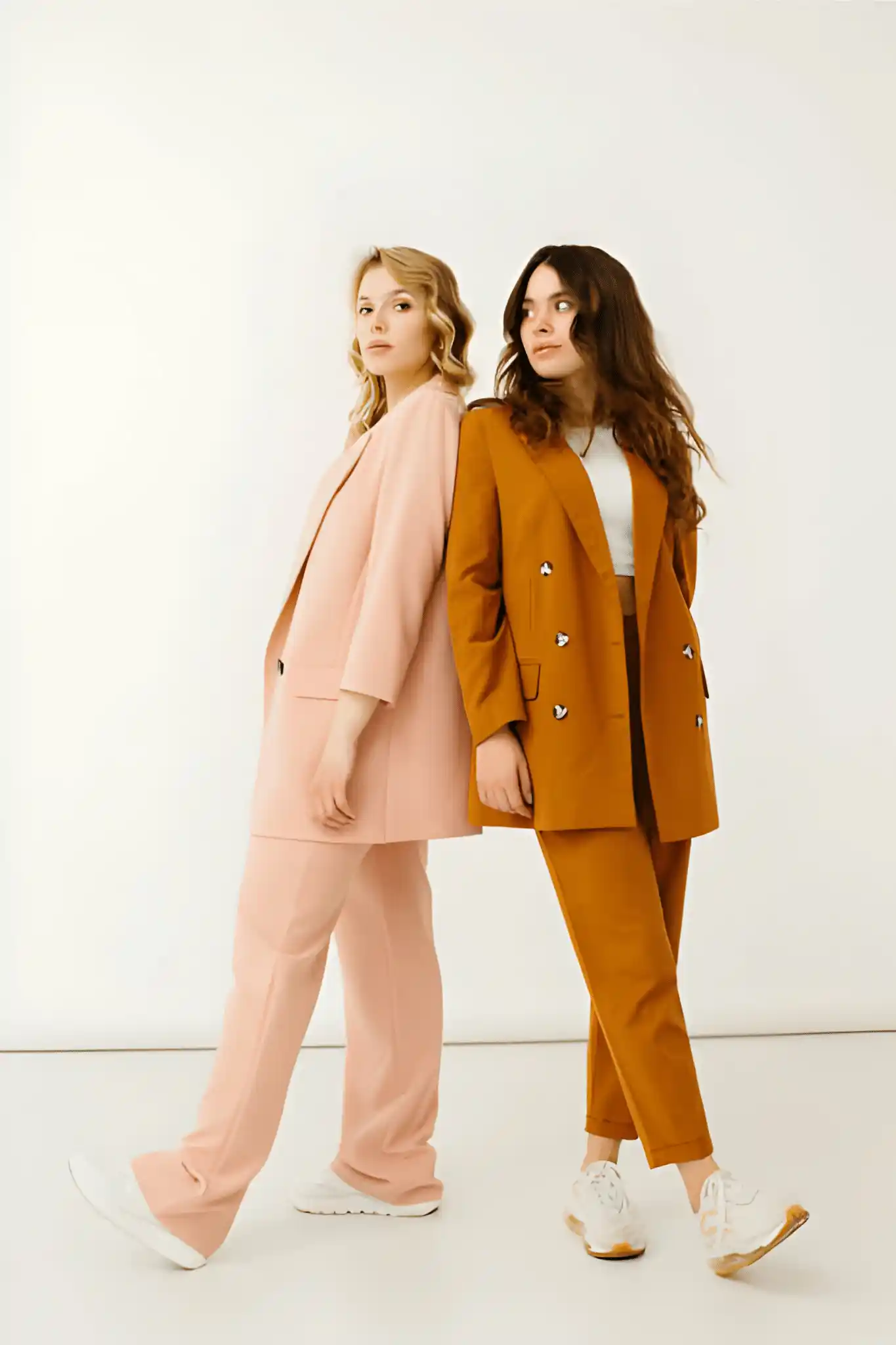 Two models wearing tailored blush pink and ochre suits