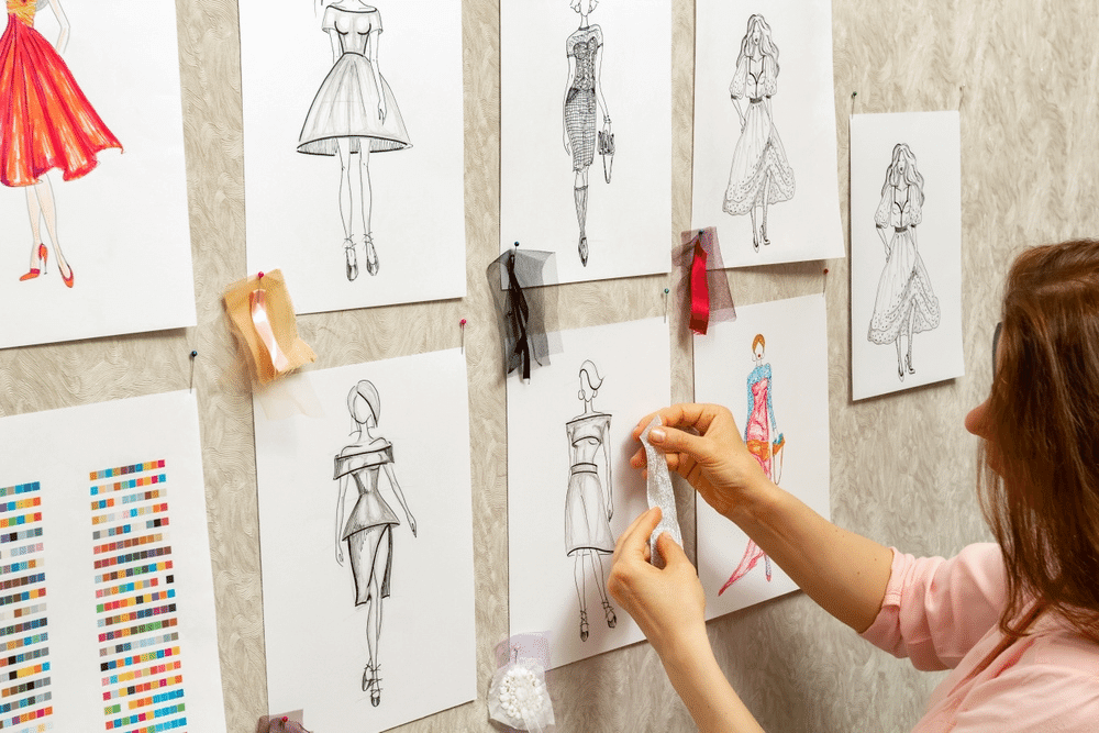 A stylist who hangs women's dress designs on a corkboard.
