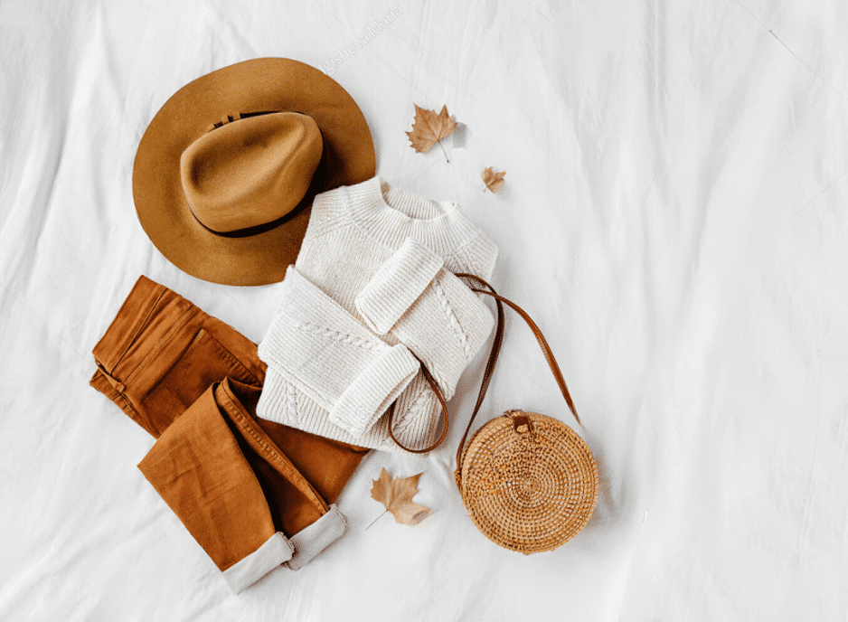 A white background featuring a bamboo fabric hat, sweater, pants, bag, and decorative leaves.
